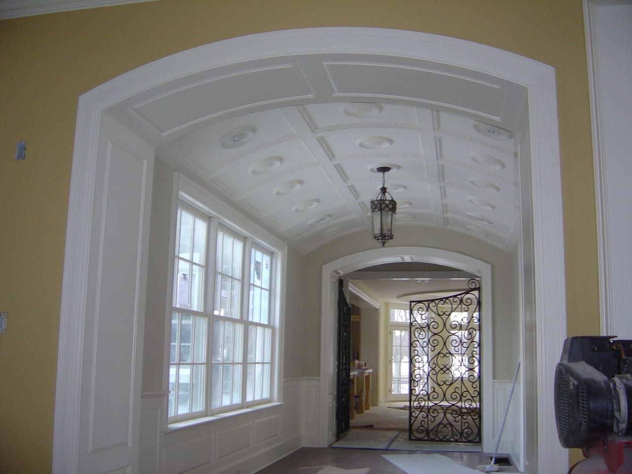 Barrel-vaulted gallery with a painted coffered ceiling, paneled walls and an arched doorway, painted by Campbell McHugh