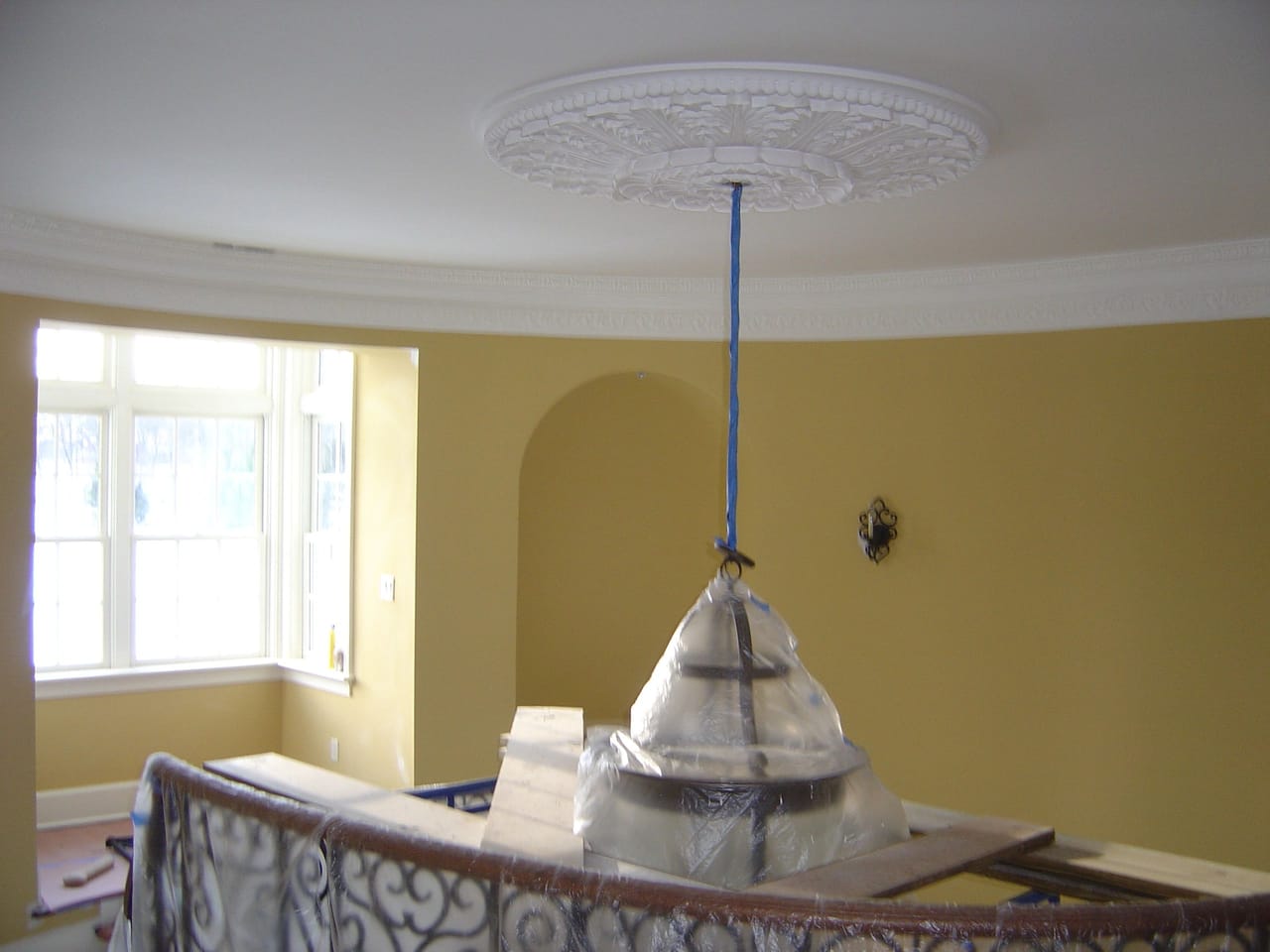 Curved rotunda with an ornate plaster ceiling medallion and crown molding, mid-project with the chandelier still wrapped